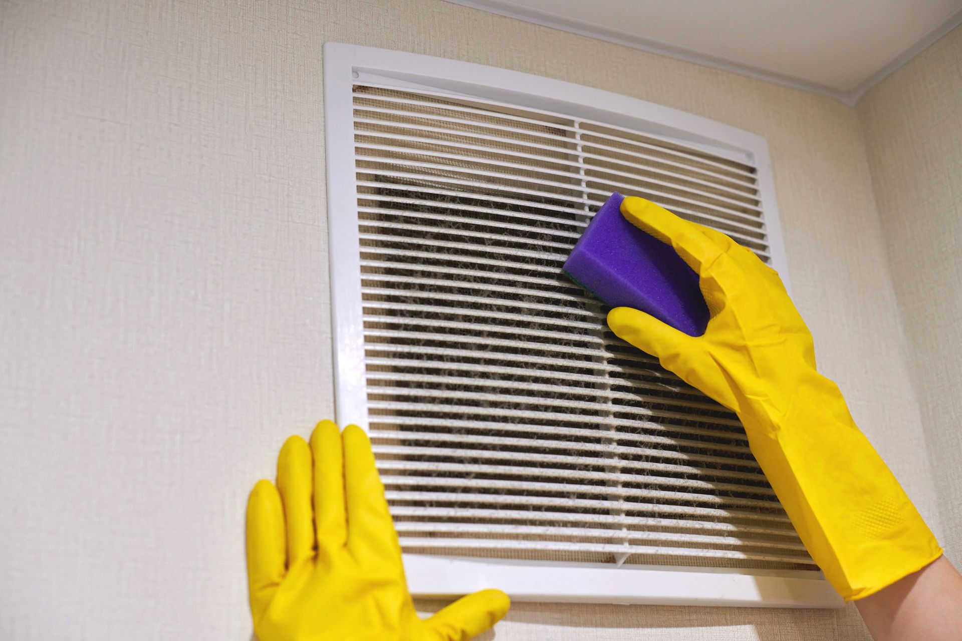 Person cleaning a white vent with a purple cloth while wearing yellow gloves