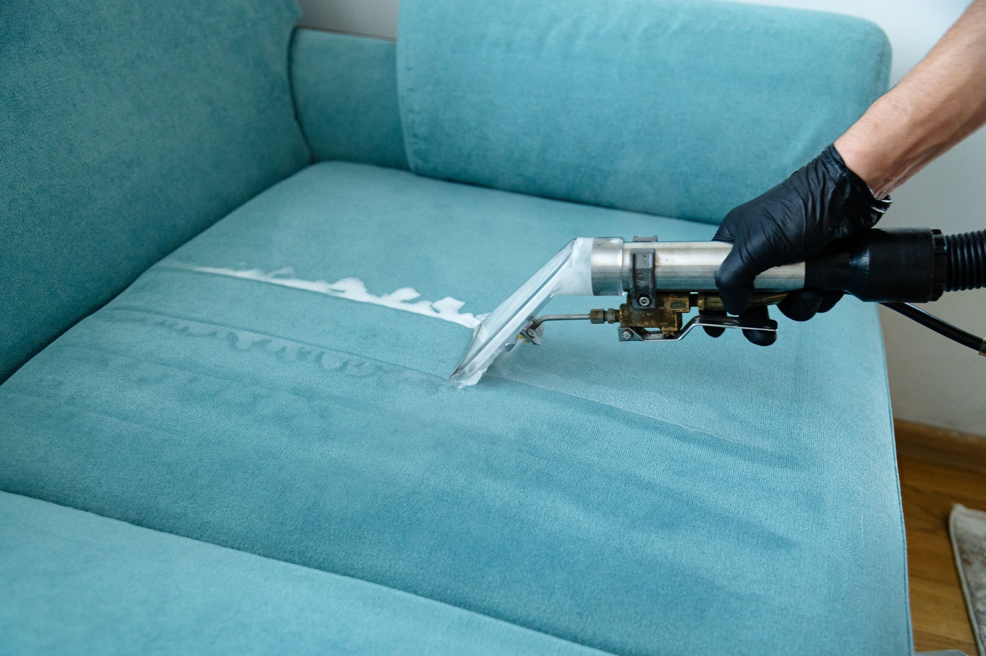 Person steam-cleaning a light blue couch with a handheld upholstery vacuum