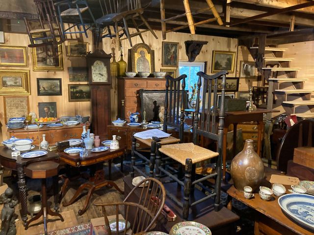 A narrow room features antique wood furniture, ornate vases, and framed oil portraits on cream-colored walls.