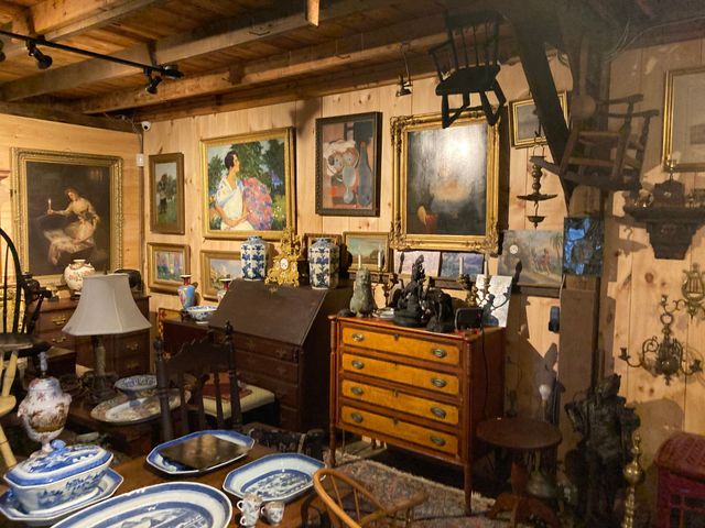 Martin's Antiques shop with a green door and trim, white siding, and windows displaying framed artwork and vases.