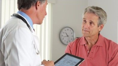 A doctor is talking to a patient while holding a tablet.