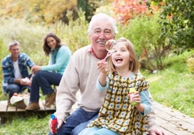 A little girl is blowing soap bubbles with her grandfather.