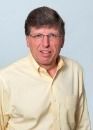 A man wearing glasses and a yellow shirt is smiling for the camera.