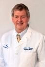A man in a white lab coat and tie is smiling.