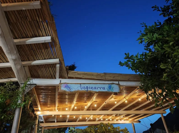 Pergola in legno con luci decorative e insegna blu sullo sfondo di un cielo serale luminoso.