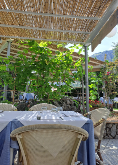 Tavolini da caffè all'aperto con sedie in vimini, tovaglie blu e un tetto di bambù ombreggiante con vista sul verde e sulle montagne.
