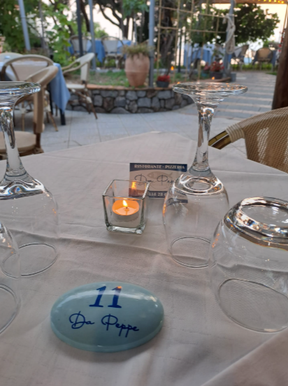 Tavolo da ristorante apparecchiato con bicchieri d'acqua, candela e biglietto d'auguri blu per l'anniversario su una tovaglia bianca.