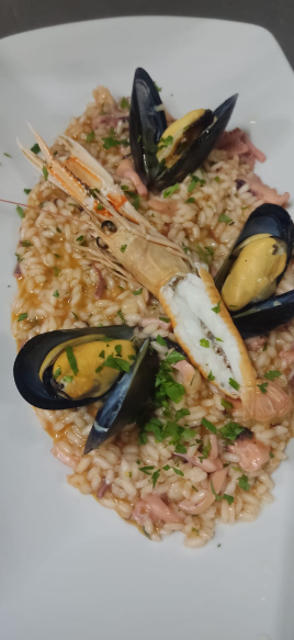 Risotto ai frutti di mare con cozze, gamberi e calamari, servito su un piatto bianco.