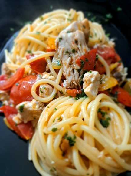 Spaghetti al sugo di pomodoro, erbe aromatiche e pollo sminuzzato su un piatto scuro
