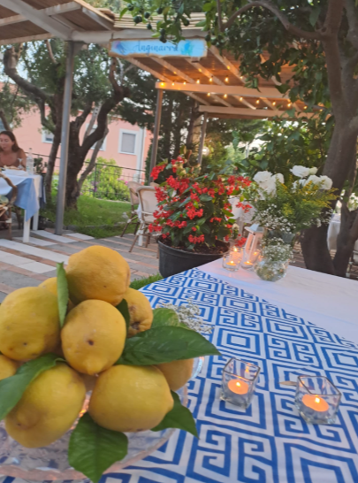 Limoni in una ciotola su una tovaglia blu a motivi geometrici, con candele e fiori in un'ambientazione da giardino.