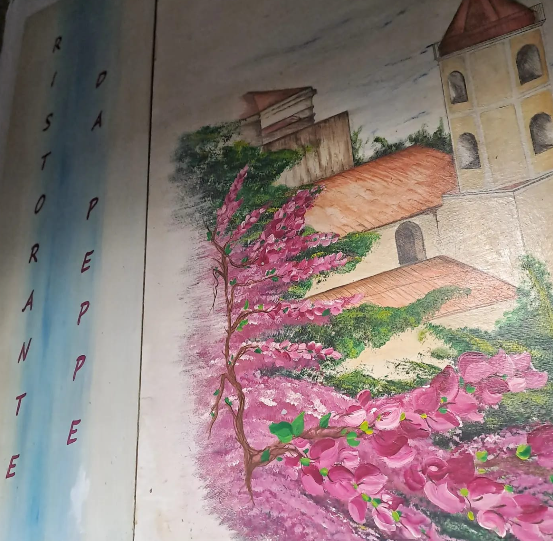Un murale disegnato a mano raffigurante fiori rosa, fogliame verde ed edifici con tetti di terracotta e una torre.
