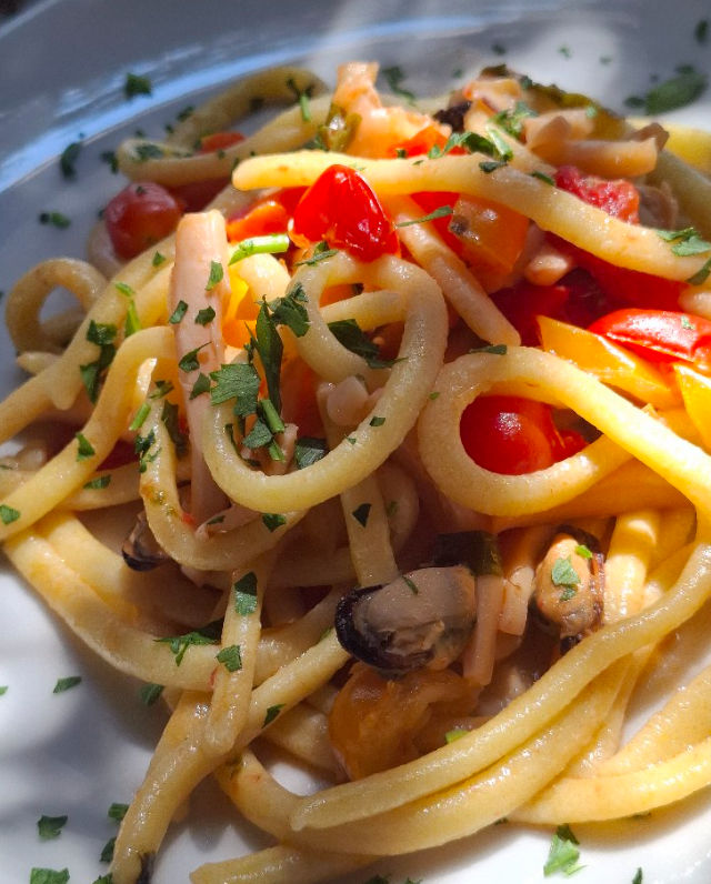 Pasta con pomodorini, funghi ed erbe aromatiche in una ciotola bianca, condita con olio d'oliva.
