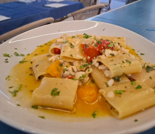 Piatti di pasta a forma di tubi in salsa d'arancia, guarniti con erbe aromatiche, formaggio e pomodorini, disposti su un tavolo di ristorante.