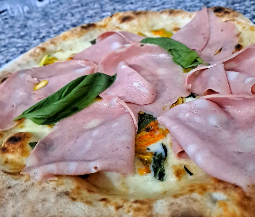 Pizza condita con fette di prosciutto rosa e basilico fresco su una crosta dorata