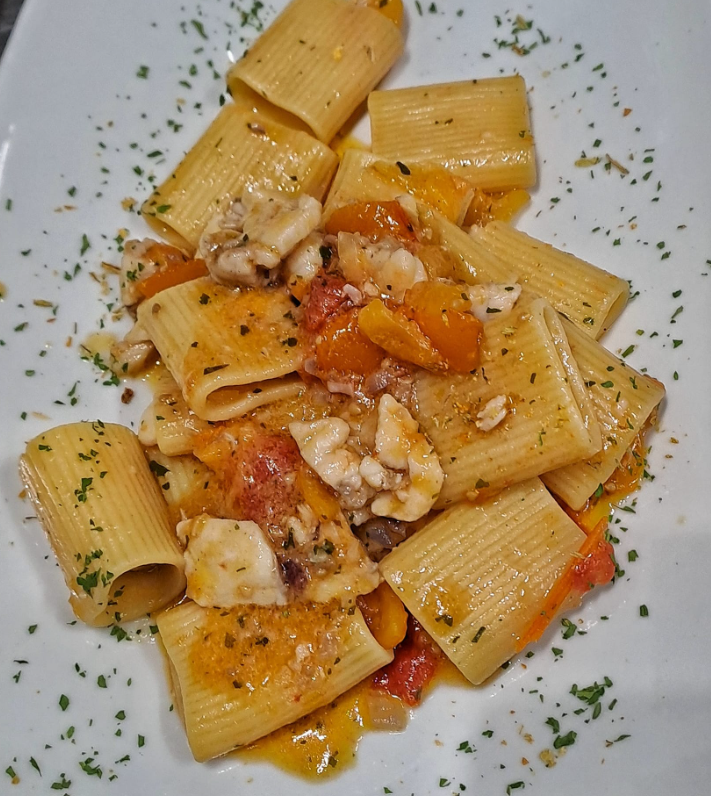 Rigatoni con salsa di pomodoro ed erbe aromatiche su un piatto bianco.