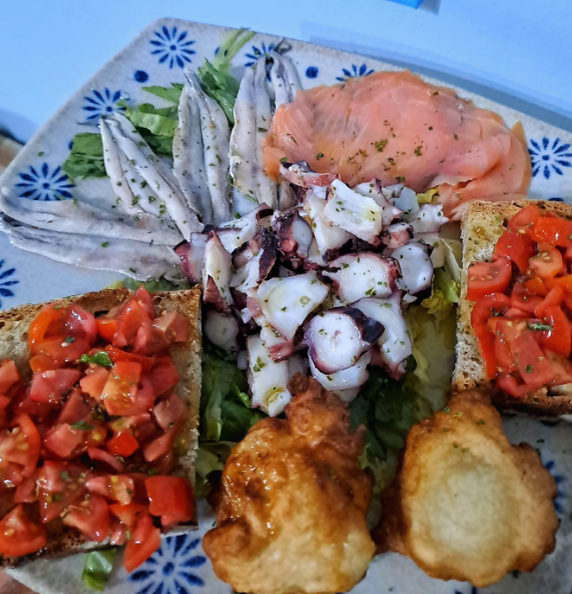 Antipasti misti di frutti di mare con gamberi, polpo, pomodori e pezzi fritti su un piatto decorativo.