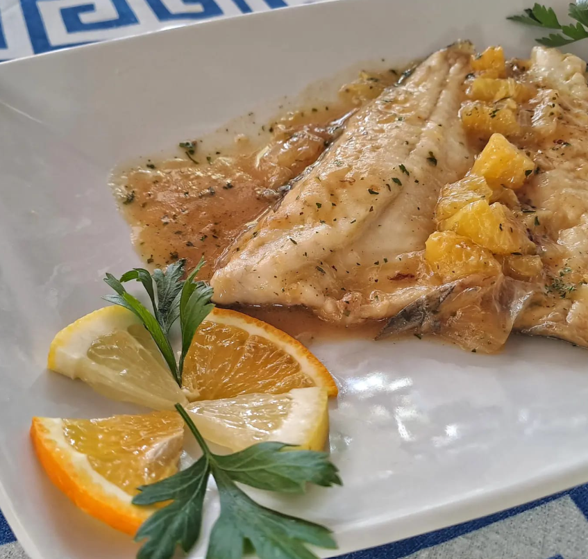 Pesce grigliato servito con salsa, pezzi di ananas, fette di limone e guarnizione di prezzemolo.