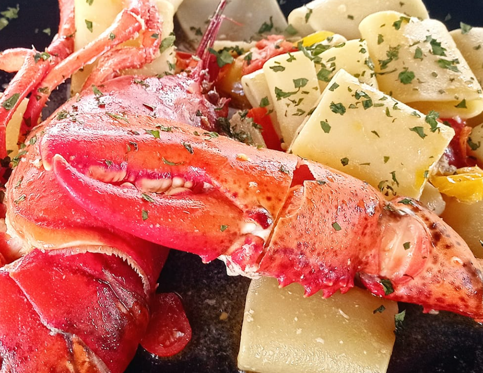 Chele di aragosta e patate alle erbe aromatiche su un piatto, primo piano di un pasto a base di pesce.