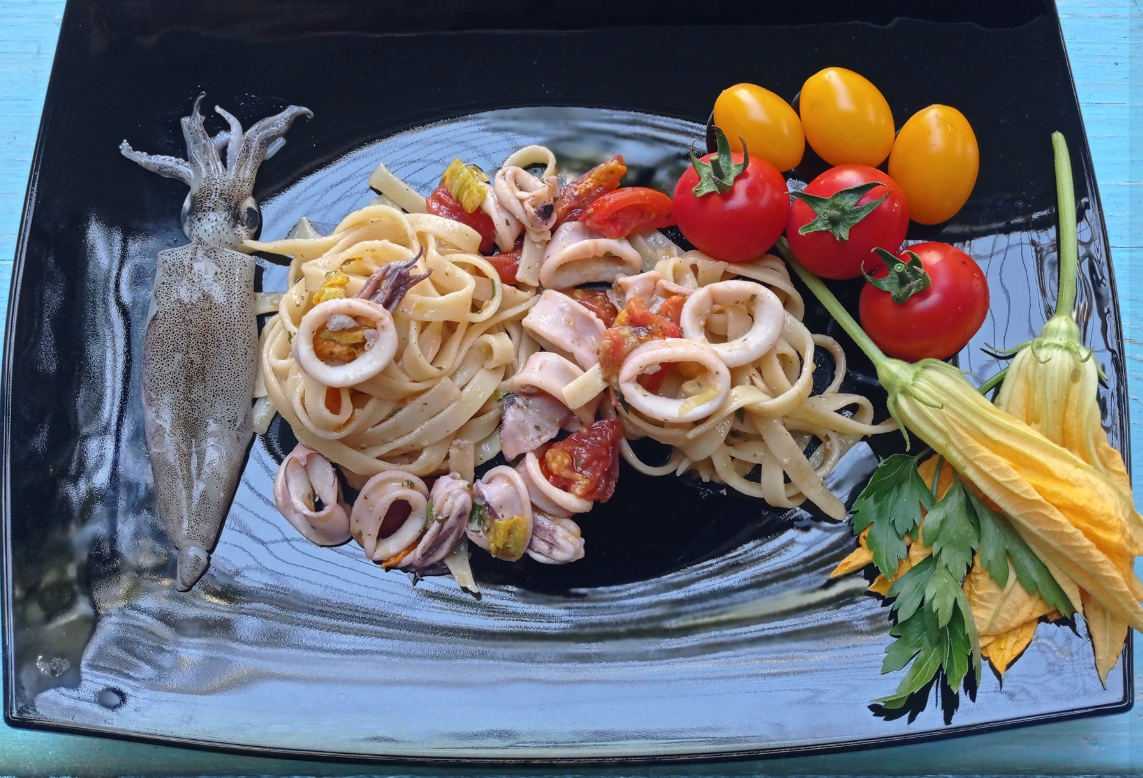 Pasta con calamari grigliati, pomodorini e limone su un piatto nero, guarnita con prezzemolo e mais.