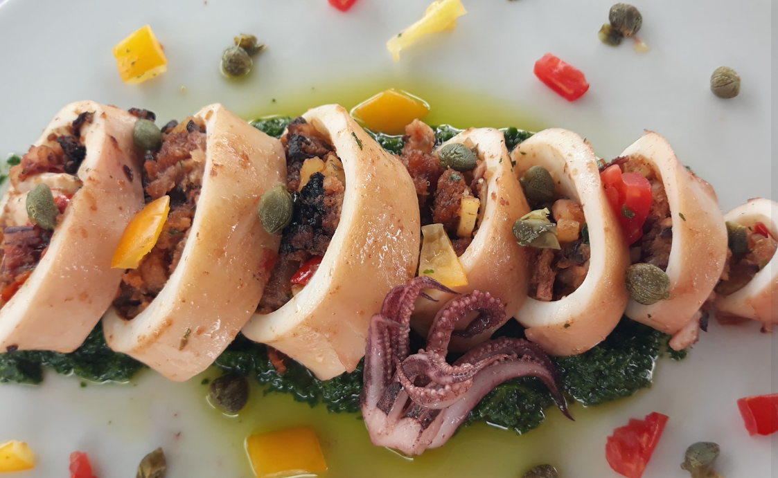 Calamari ripieni a fette con guarnizione colorata e salsa, serviti su un piatto bianco.