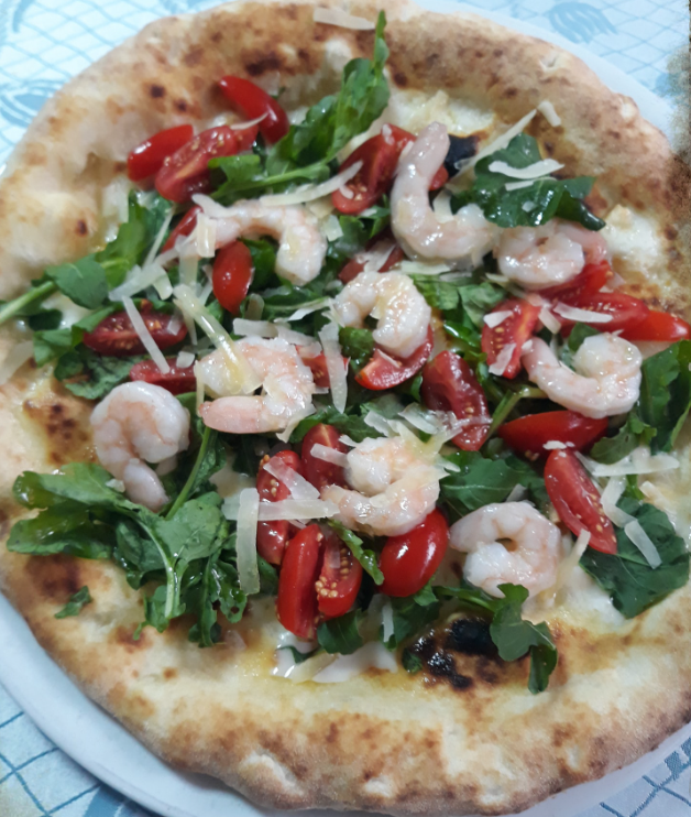 Pizza con gamberi e rucola, pomodorini e salsa bianca, servita su un piatto.
