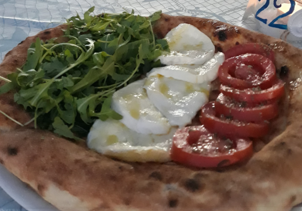 Pizza su pane piatto con rucola, formaggio fuso e pomodori a fette, servita su carta in un cestino.