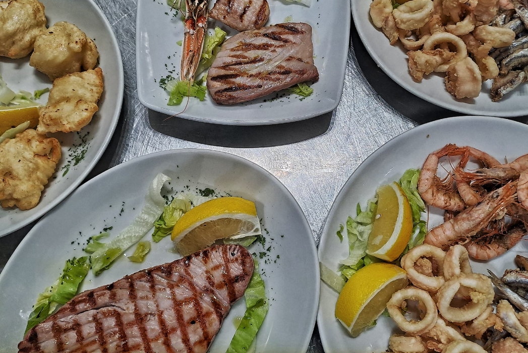 Piatti di frutti di mare e pesce grigliati con spicchi di limone, disposti su un tavolo.