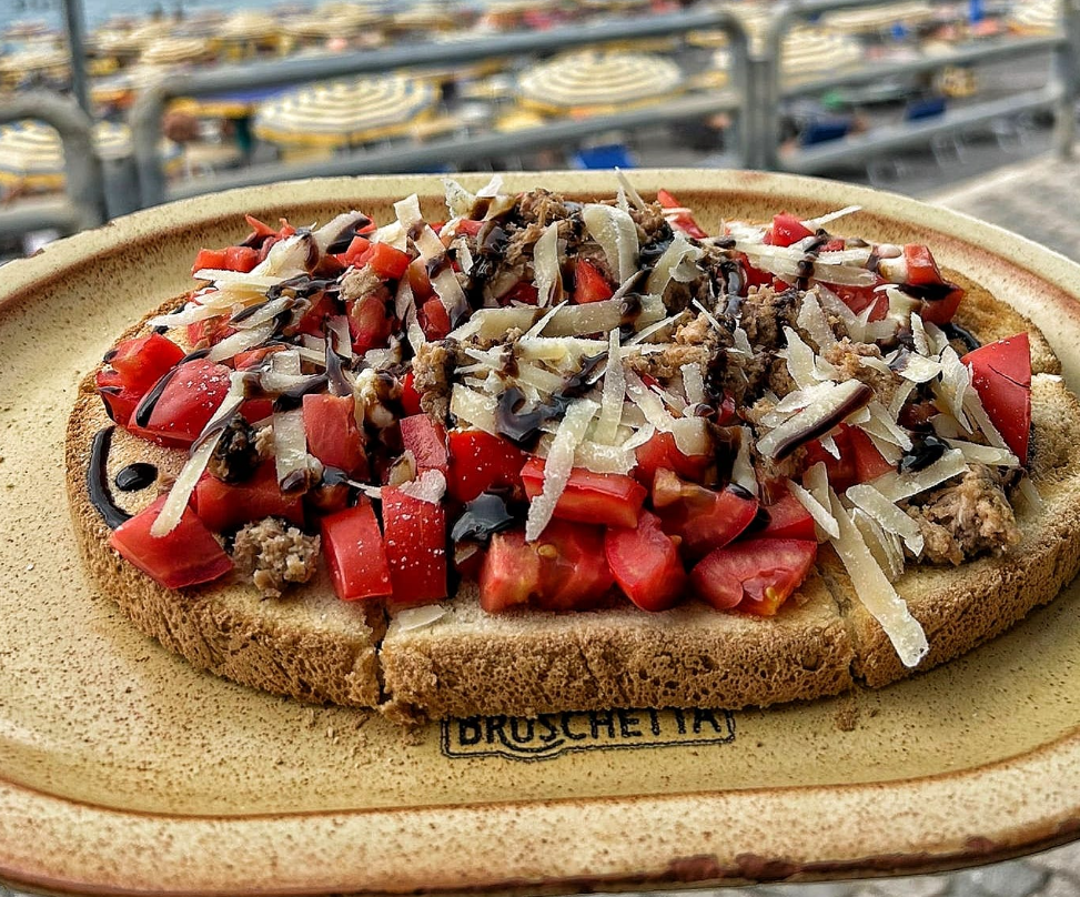 Focaccia in stile bruschetta condita con pomodori, olive e formaggio grattugiato, servita su un piatto.