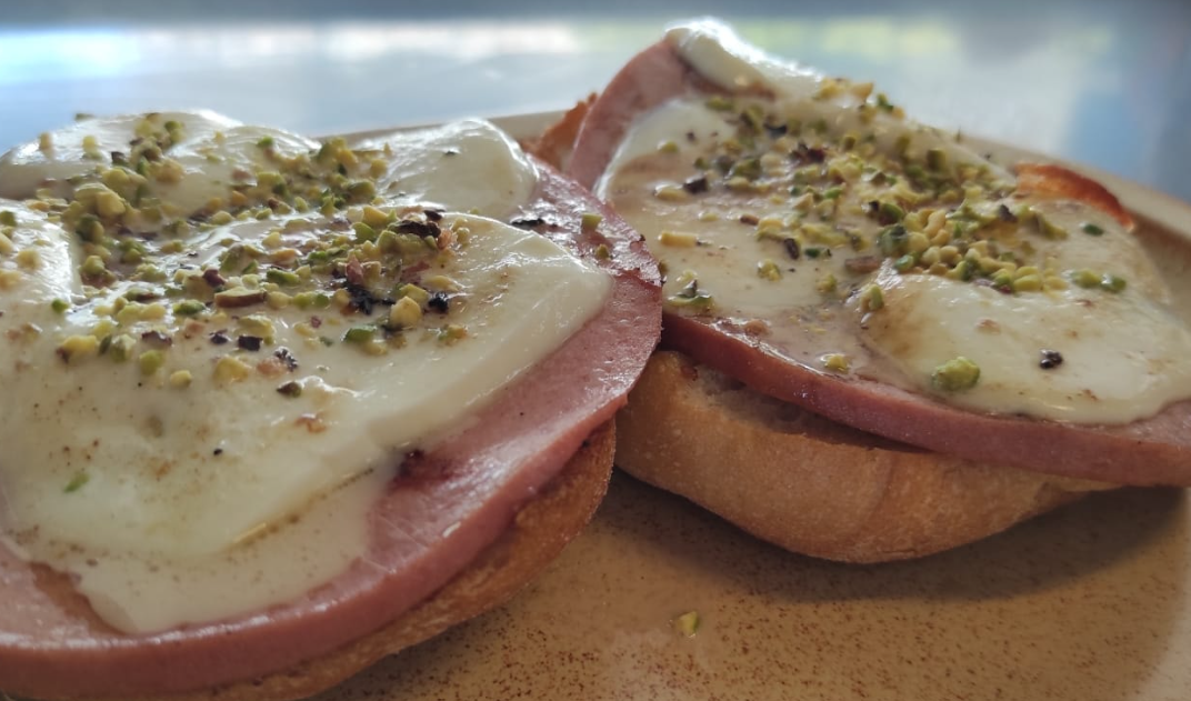 Due fette di pane tostato con formaggio fuso ed erbe aromatiche su un tagliere di legno.