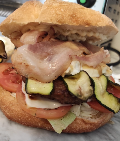 Primo piano di un cheeseburger con pancetta, pomodori, lattuga e zucchine grigliate in un panino.