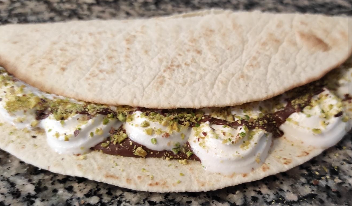 Panino pita con hummus, cipolle a fette e guarnizione verde su un piano di lavoro in granito.