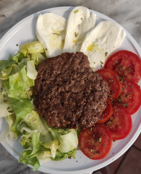 Piatto unico con hamburger, insalata, fette di pomodoro e mozzarella con olio d'oliva.