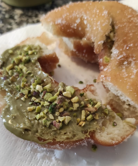 Ciambella ricoperta di crema verde al pistacchio e pistacchi tritati, servita su un piatto bianco.