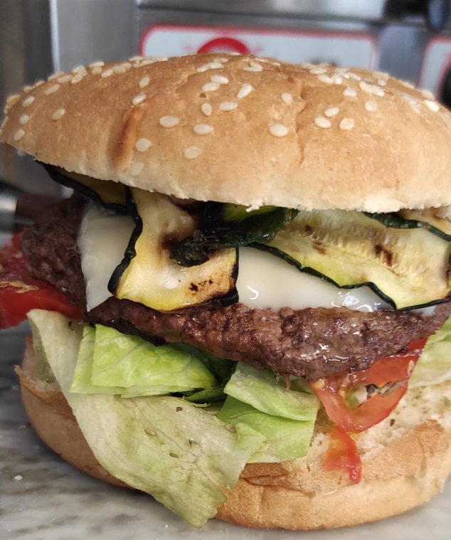 Cheeseburger con semi di sesamo, lattuga, pomodoro e zucchine grigliate in un panino.