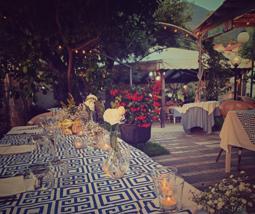 Un'atmosfera romantica per cenare all'aperto, con tavoli illuminati da candele, tovaglie decorate, fiori e luci decorative in un giardino.