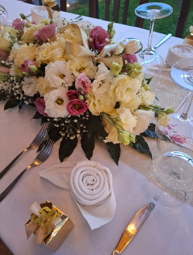 Centrotavola floreale di fiori bianchi e rosa su una tavola decorata con tovagliolo piegato e bicchieri.