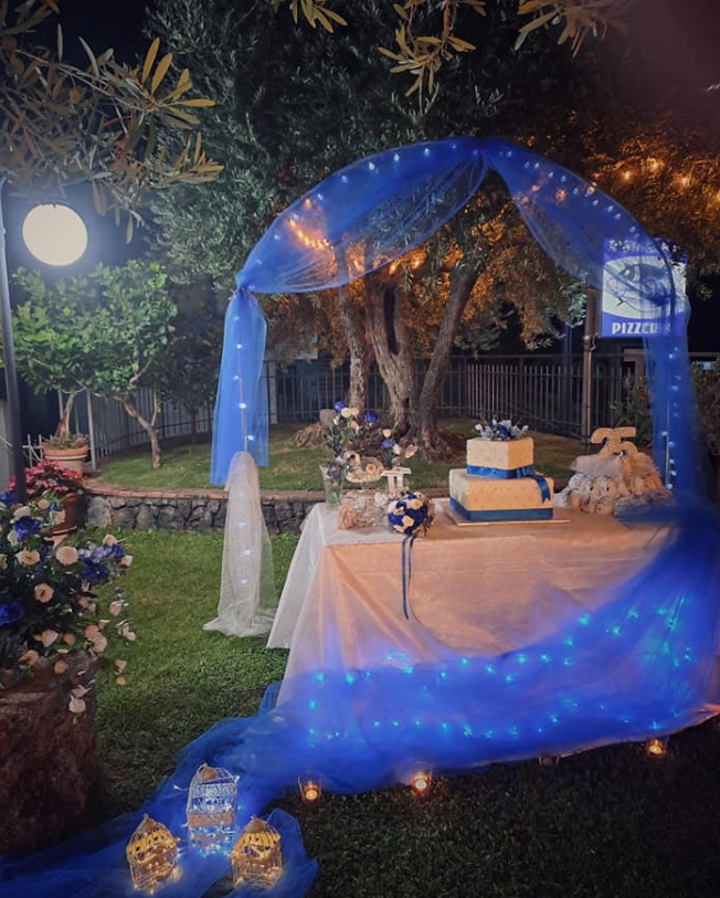 Tavolo da dessert all'aperto illuminato di blu sotto un arco luminoso in un giardino di notte
