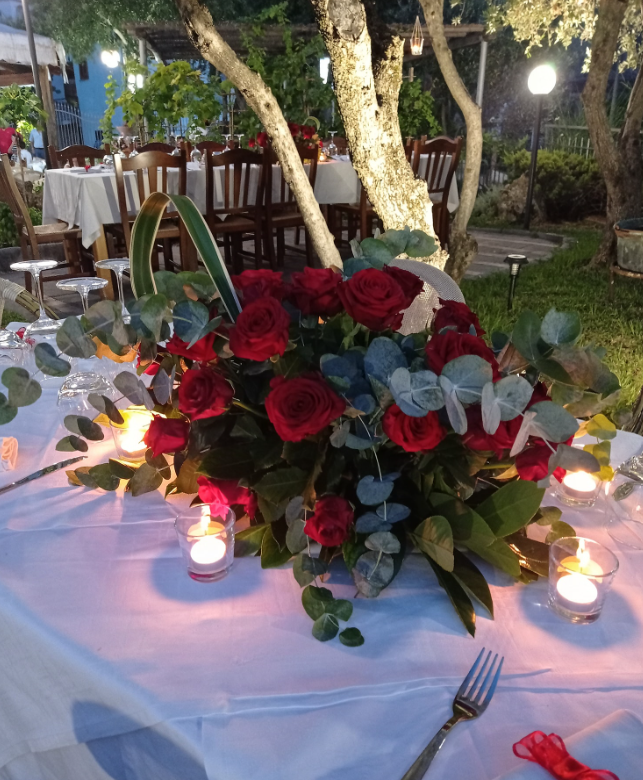 Centrotavola di rose rosse con candele su un tavolo da pranzo all'aperto ricoperto di drappeggi bianchi, di sera.
