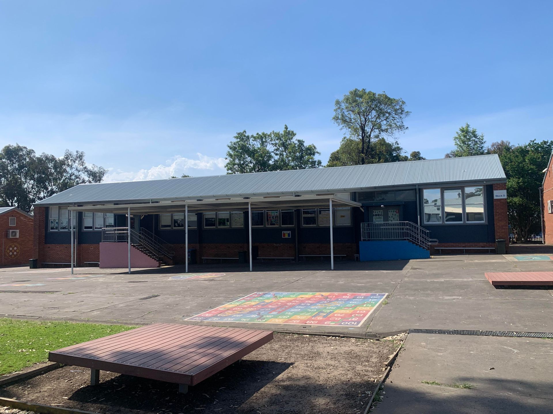 A school building with a rainbow painting on the ground in front of it — Kimick Roofing Solutions In Wyong, NSW
