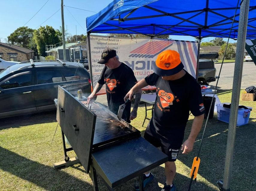 Two men are cooking on a grill under a blue tent — Kimick Roofing Solutions In Wyong, NSW