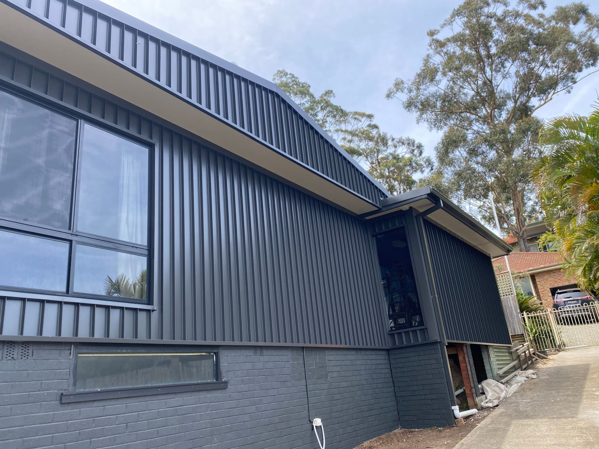 A black house with a lot of windows is sitting on top of a hill — Kimick Roofing Solutions In Wyong, NSW
