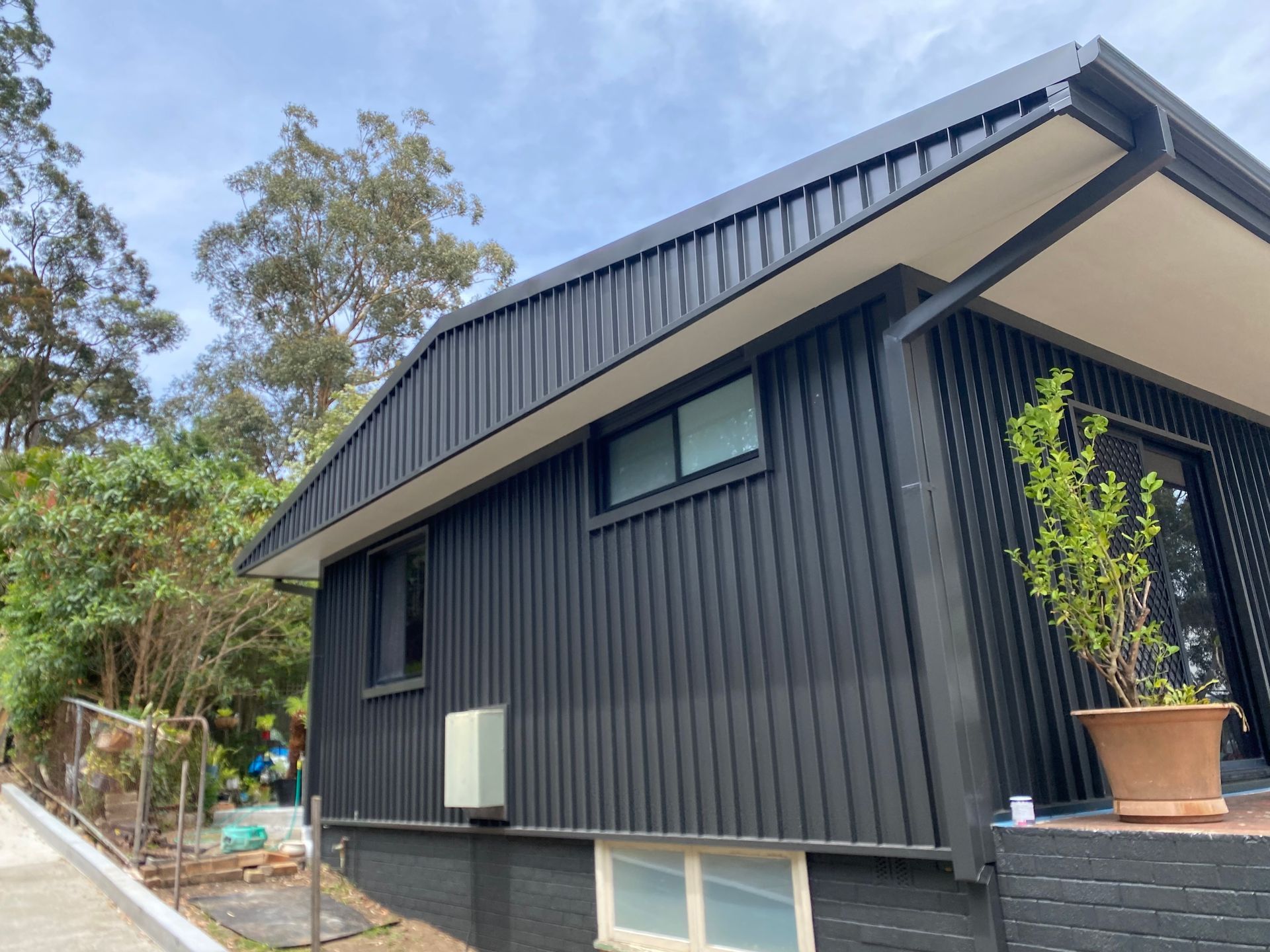 A black house with a white roof and a potted plant in front of it — Kimick Roofing Solutions In Wyong, NSW