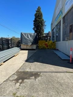 A large dumpster is sitting in a parking lot next to a building — Kimick Roofing Solutions In Wyong, NSW