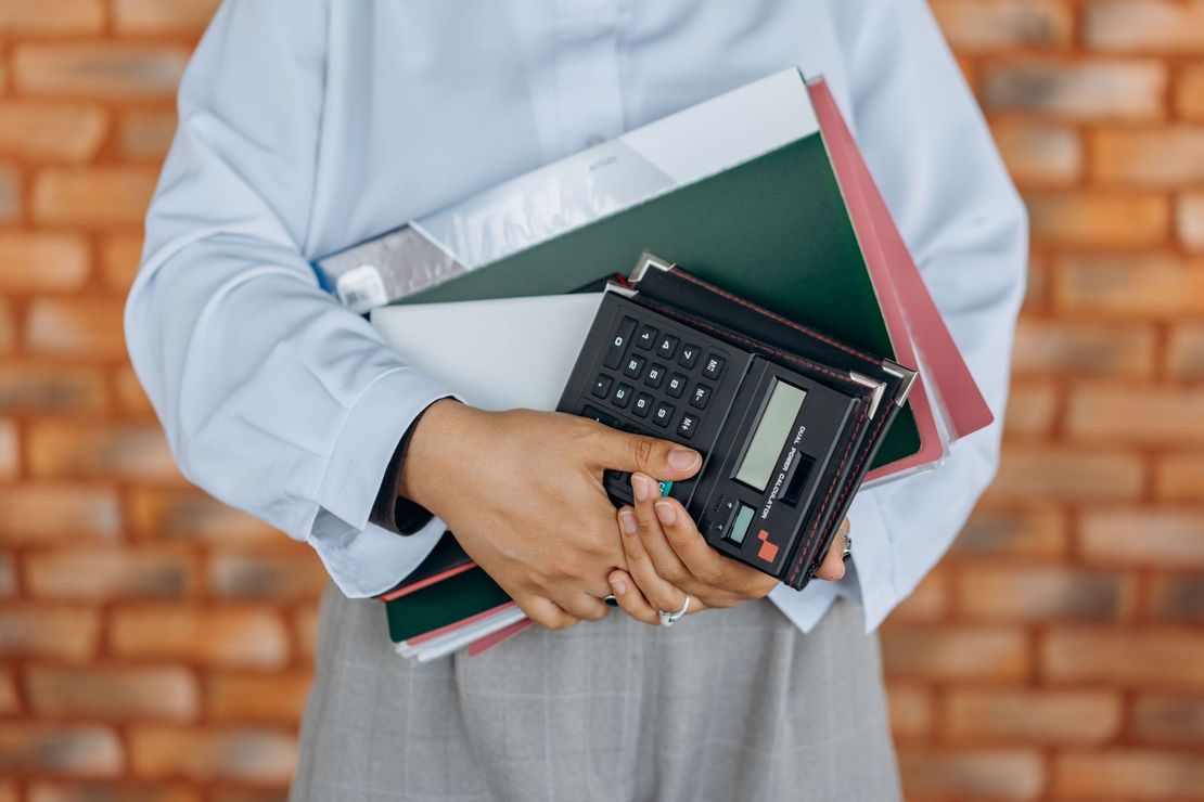 Person holding folders and a calculator against a light background