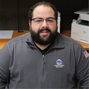 Portrait of a man with glasses and beard wearing a gray zip-up pullover in an office setting