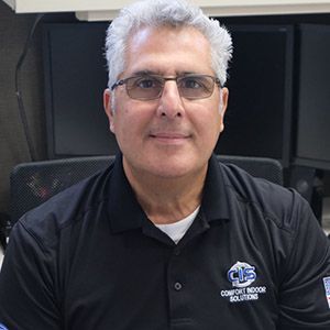 Man in glasses and black polo shirt seated in an office, smiling at the camera.