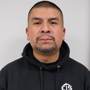 Man in black hoodie against a plain gray background, facing the camera.