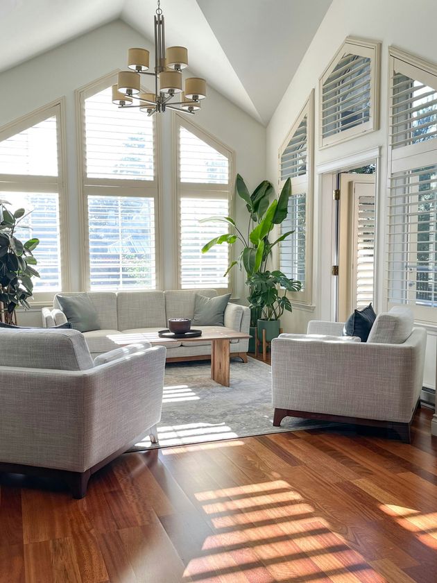 Bright living room with vaulted ceiling, gray chairs, white sofa, large windows, and sunlight on wood floors
