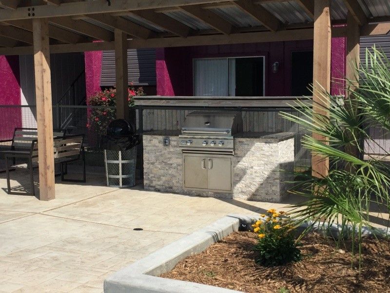 Outdoor patio with grill, stone counter, and potted plants under a pergola.