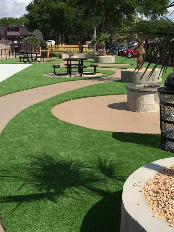 Curved green and tan playground path with picnic table, trees, and benches in a park